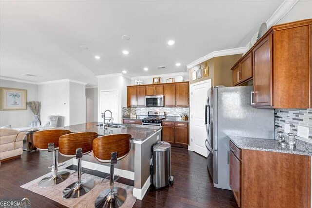 kitchen with a kitchen breakfast bar, sink, light stone countertops, an island with sink, and stainless steel appliances