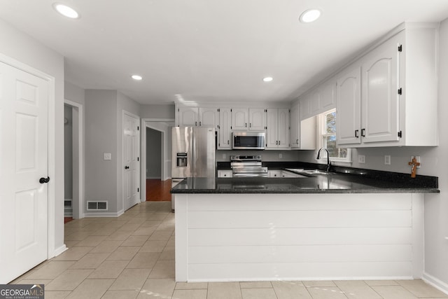 kitchen with kitchen peninsula, sink, light tile patterned flooring, white cabinetry, and appliances with stainless steel finishes