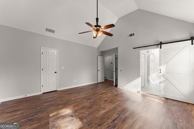 unfurnished bedroom featuring ceiling fan, a barn door, ensuite bath, dark wood-type flooring, and high vaulted ceiling