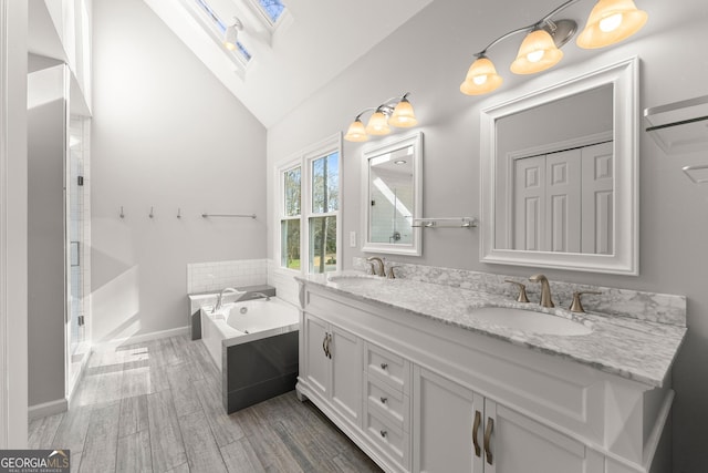 bathroom with vaulted ceiling with skylight, shower with separate bathtub, wood-type flooring, and vanity