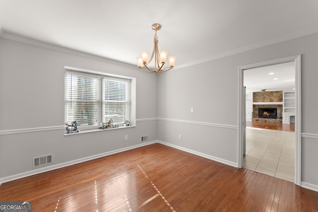 unfurnished room featuring wood-type flooring, crown molding, a notable chandelier, and a fireplace