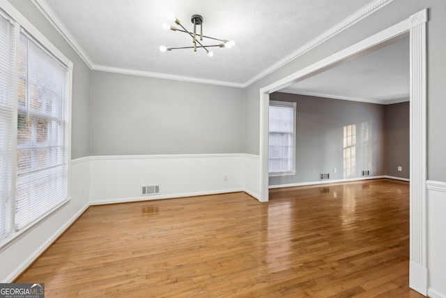 empty room with crown molding, a chandelier, and light wood-type flooring