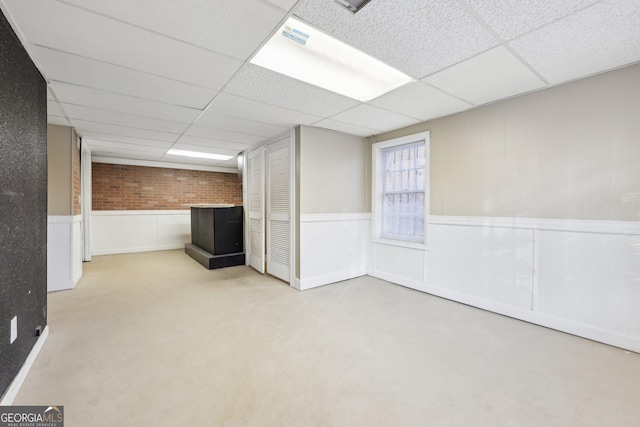 basement featuring a drop ceiling and brick wall