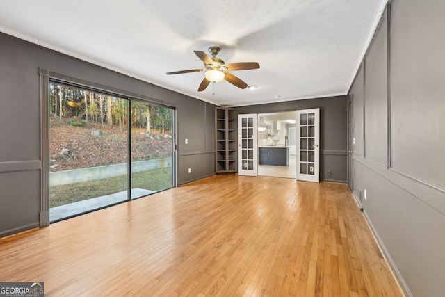 unfurnished living room with ceiling fan, french doors, ornamental molding, and light wood-type flooring