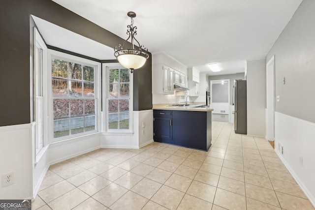 kitchen with white cabinets, stainless steel fridge, light tile patterned floors, blue cabinetry, and decorative light fixtures