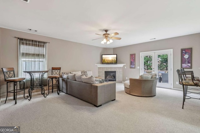 living room featuring a tile fireplace, light carpet, french doors, and ceiling fan