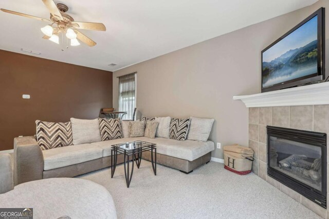 carpeted living room with a tile fireplace and ceiling fan