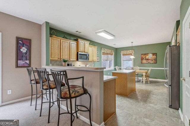 kitchen with a center island, a kitchen breakfast bar, hanging light fixtures, appliances with stainless steel finishes, and kitchen peninsula