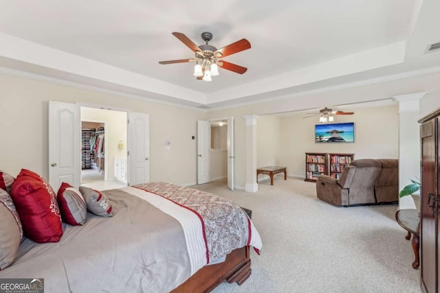 bedroom with ceiling fan, a raised ceiling, decorative columns, light colored carpet, and a walk in closet