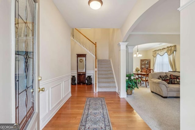 entryway featuring ornate columns, hardwood / wood-style floors, an inviting chandelier, and ornamental molding