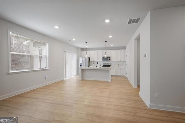 kitchen with white cabinets, pendant lighting, stainless steel appliances, and a center island with sink