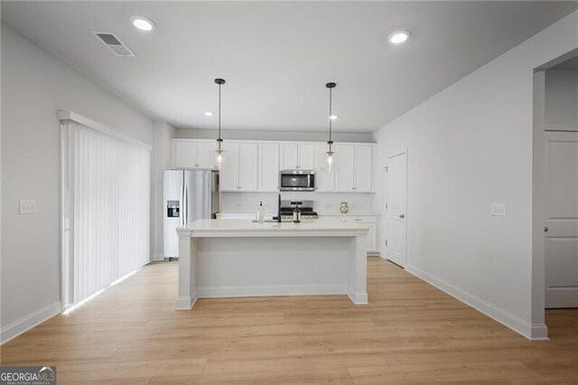 kitchen featuring white cabinetry, stainless steel appliances, light hardwood / wood-style flooring, pendant lighting, and a center island with sink