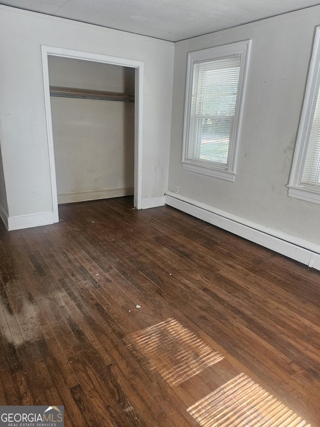 unfurnished bedroom with dark wood-type flooring, baseboard heating, and a closet