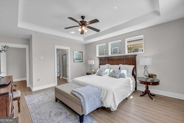 bedroom featuring ceiling fan, light hardwood / wood-style floors, and a tray ceiling