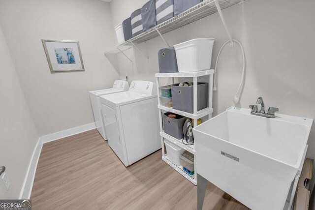 clothes washing area featuring washing machine and dryer, light hardwood / wood-style flooring, and sink