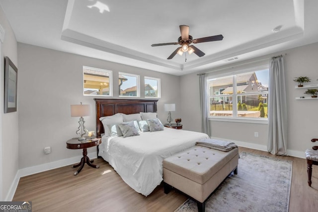 bedroom featuring light wood-type flooring, a raised ceiling, and ceiling fan