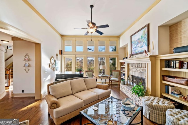 living room featuring ceiling fan, a towering ceiling, dark wood-type flooring, and a brick fireplace