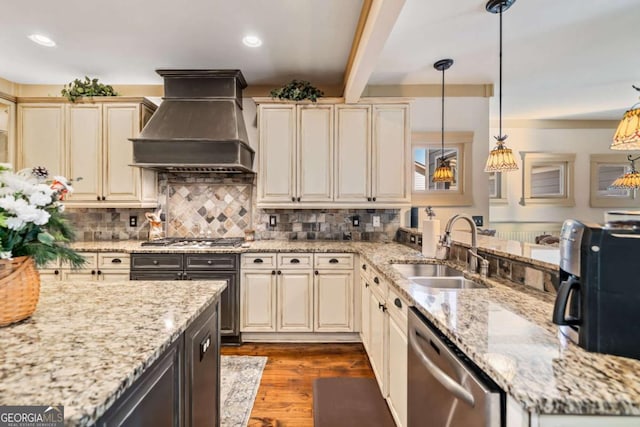 kitchen featuring sink, stainless steel appliances, premium range hood, cream cabinets, and decorative light fixtures