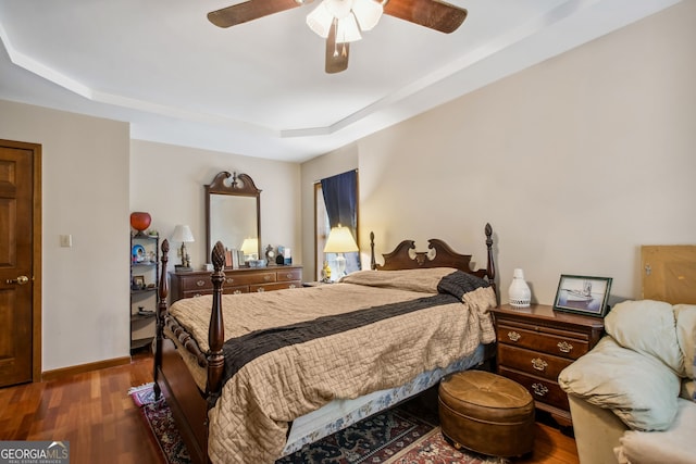 bedroom with a raised ceiling, ceiling fan, and dark wood-type flooring