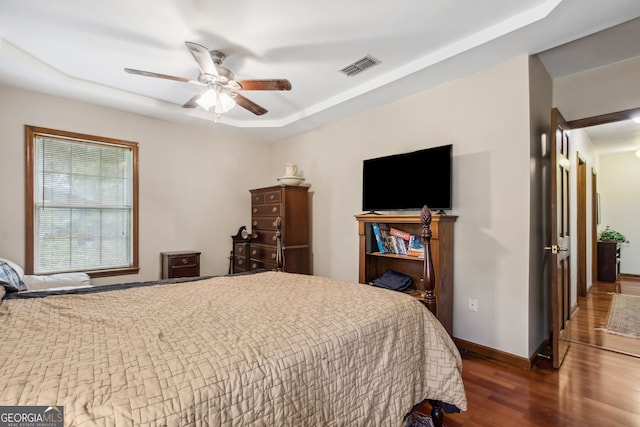 bedroom with ceiling fan, dark wood-type flooring, and a tray ceiling