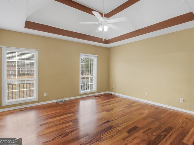 empty room with hardwood / wood-style flooring, plenty of natural light, and a tray ceiling