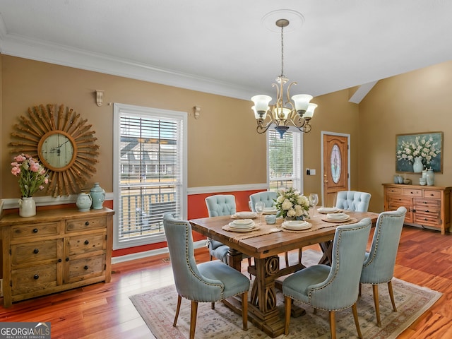 dining room with a notable chandelier, light hardwood / wood-style flooring, ornamental molding, and vaulted ceiling