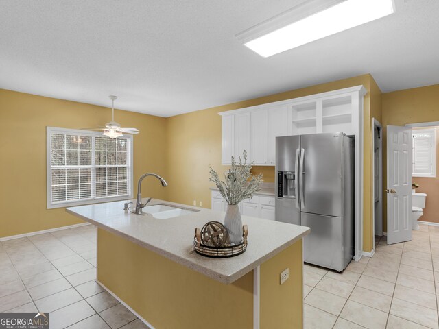 kitchen featuring stainless steel fridge, sink, a center island with sink, and white cabinets