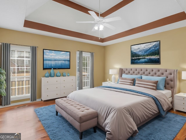 bedroom with multiple windows, a tray ceiling, light hardwood / wood-style floors, and ceiling fan