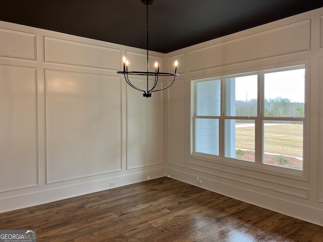 unfurnished dining area featuring a notable chandelier, a decorative wall, and dark wood-type flooring