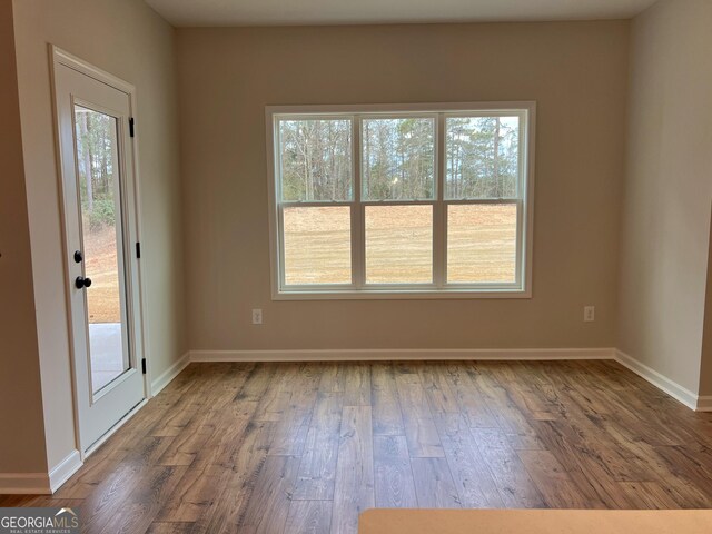 empty room with baseboards, wood finished floors, and a healthy amount of sunlight