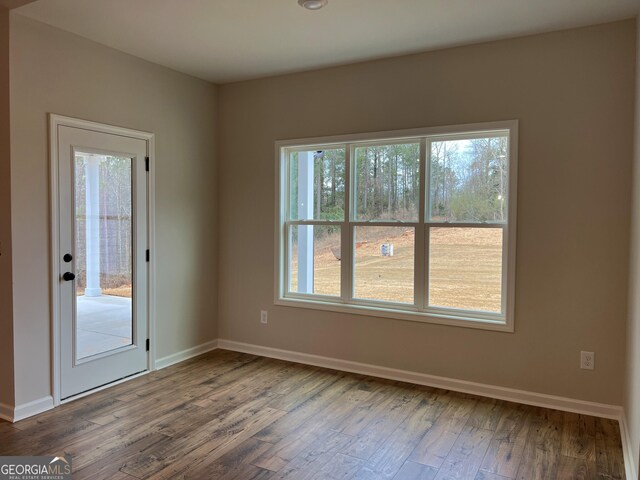 unfurnished room with a wealth of natural light, wood finished floors, and baseboards