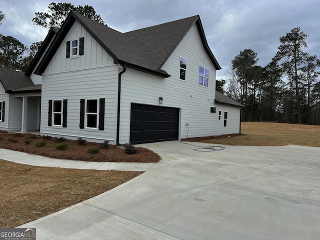 view of side of home with a garage, concrete driveway, board and batten siding, and roof with shingles