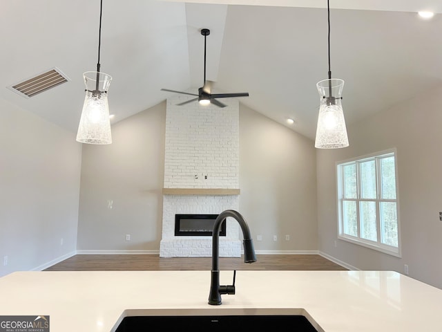 kitchen featuring visible vents, lofted ceiling, open floor plan, light countertops, and a brick fireplace