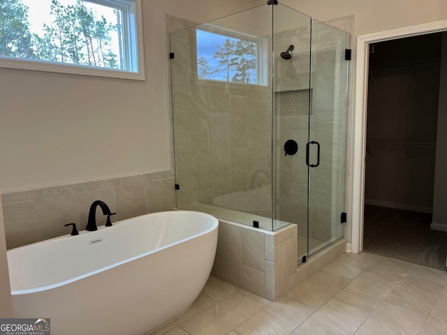 bathroom with a spacious closet, a stall shower, a soaking tub, and tile patterned floors