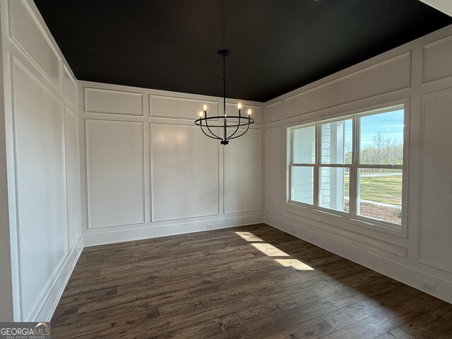 unfurnished dining area featuring an inviting chandelier, a decorative wall, and dark wood-style floors