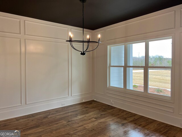 unfurnished dining area featuring dark wood finished floors, a decorative wall, and an inviting chandelier