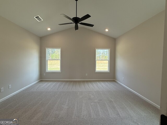 spare room with vaulted ceiling, light colored carpet, baseboards, visible vents, and a ceiling fan