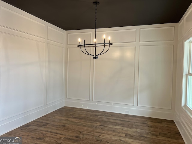 unfurnished dining area with dark wood-style floors, a chandelier, and a decorative wall