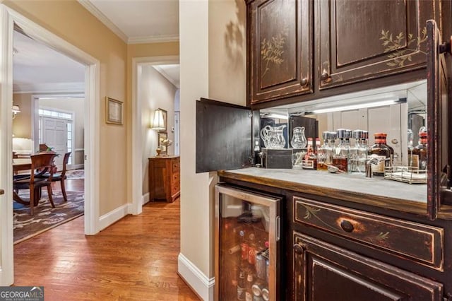 bar featuring dark brown cabinets, beverage cooler, crown molding, and hardwood / wood-style floors