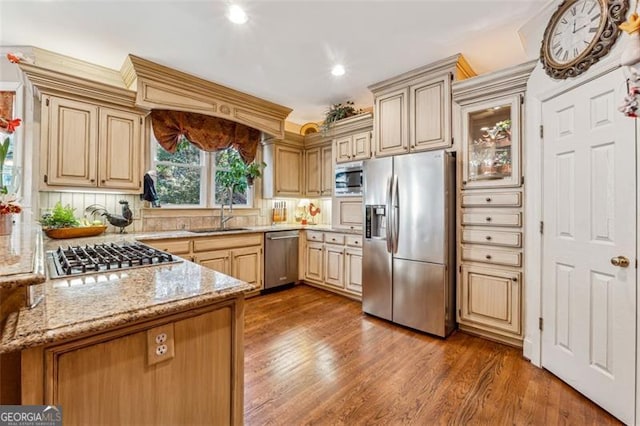 kitchen featuring decorative backsplash, light stone counters, stainless steel appliances, sink, and hardwood / wood-style flooring