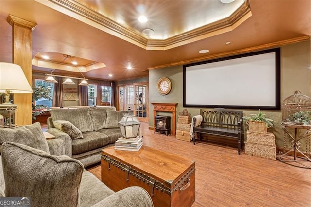 cinema room featuring a raised ceiling, a wood stove, crown molding, and hardwood / wood-style flooring