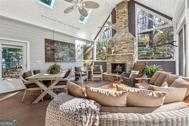 sunroom / solarium with ceiling fan, a stone fireplace, lofted ceiling with skylight, and track lighting