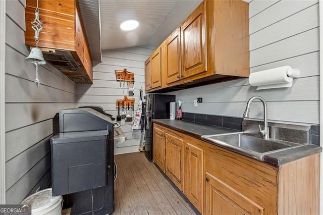 kitchen featuring sink, wood walls, light hardwood / wood-style floors, vaulted ceiling, and black refrigerator