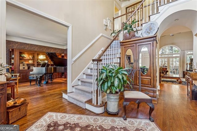 foyer with french doors, a towering ceiling, wood-type flooring, and ornamental molding