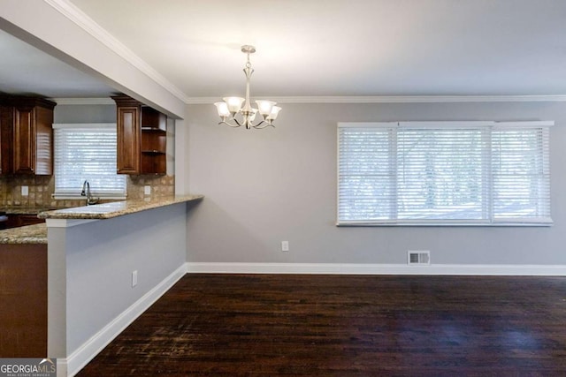 kitchen featuring hanging light fixtures, decorative backsplash, light stone countertops, ornamental molding, and a notable chandelier