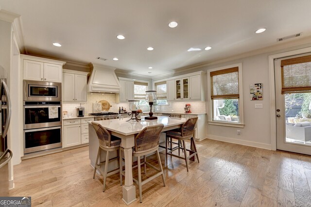 kitchen featuring appliances with stainless steel finishes, a kitchen breakfast bar, premium range hood, a kitchen island, and white cabinetry