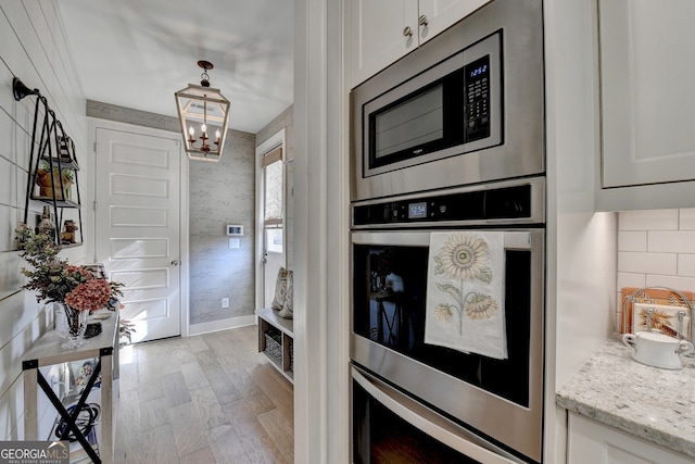 kitchen with light stone countertops, a notable chandelier, appliances with stainless steel finishes, white cabinets, and light wood-type flooring