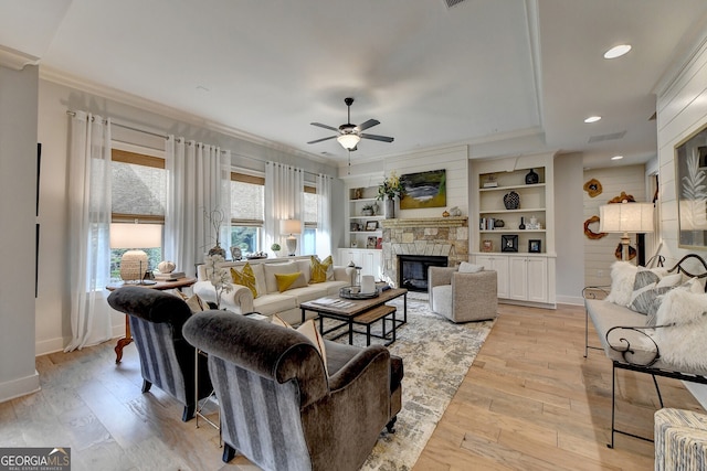 living room with crown molding, ceiling fan, light wood-type flooring, built in features, and a fireplace