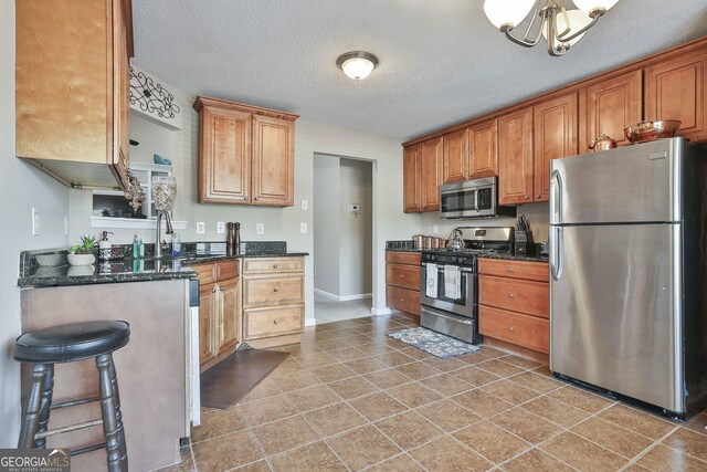 kitchen with a kitchen breakfast bar, sink, a textured ceiling, appliances with stainless steel finishes, and a notable chandelier