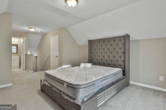 carpeted bedroom with a textured ceiling, ensuite bathroom, and vaulted ceiling